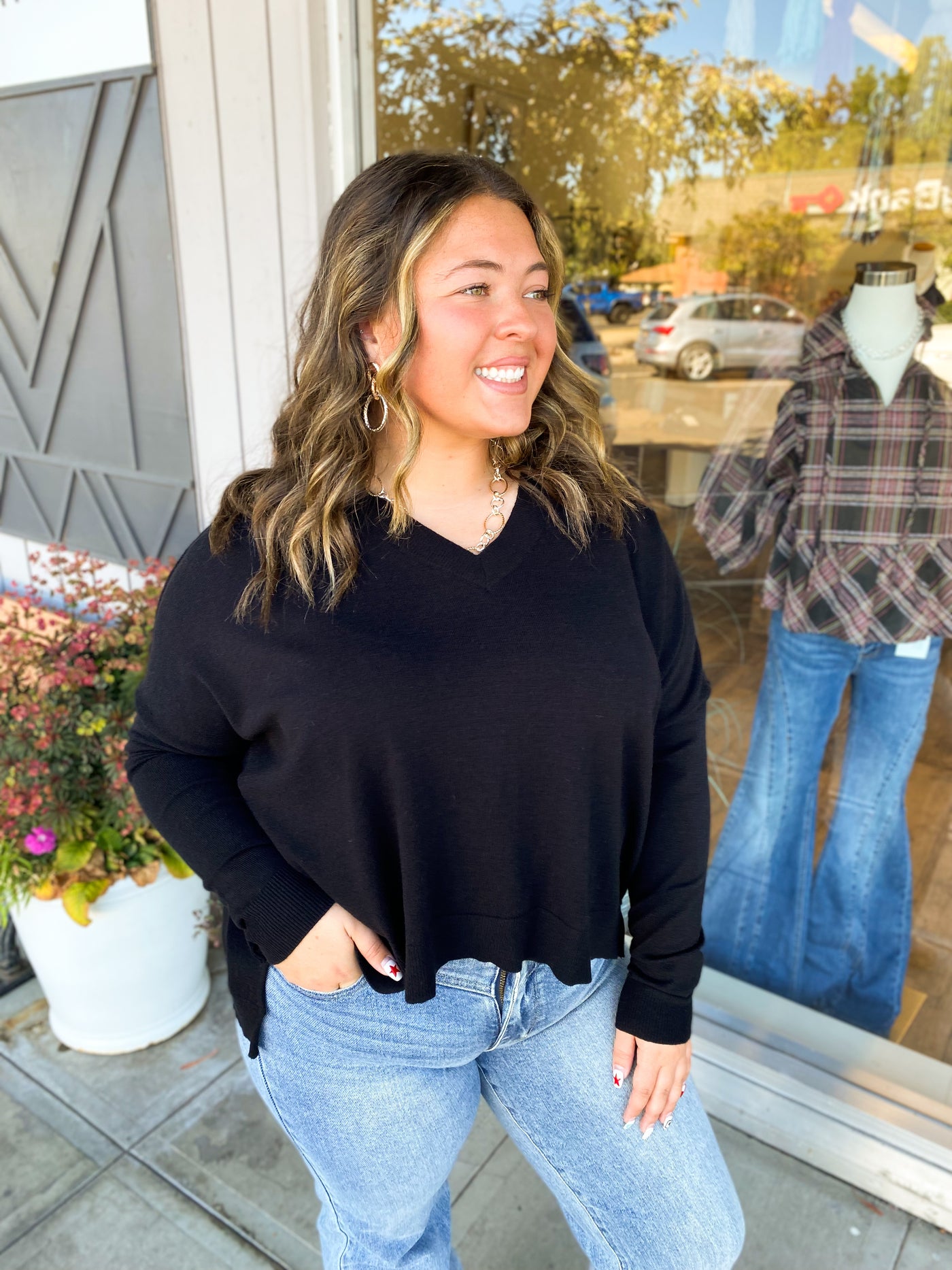 Woman wearing a black sweater and blue jeans standing outside a store.