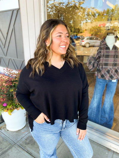 Woman wearing a black sweater and blue jeans standing outside a store.